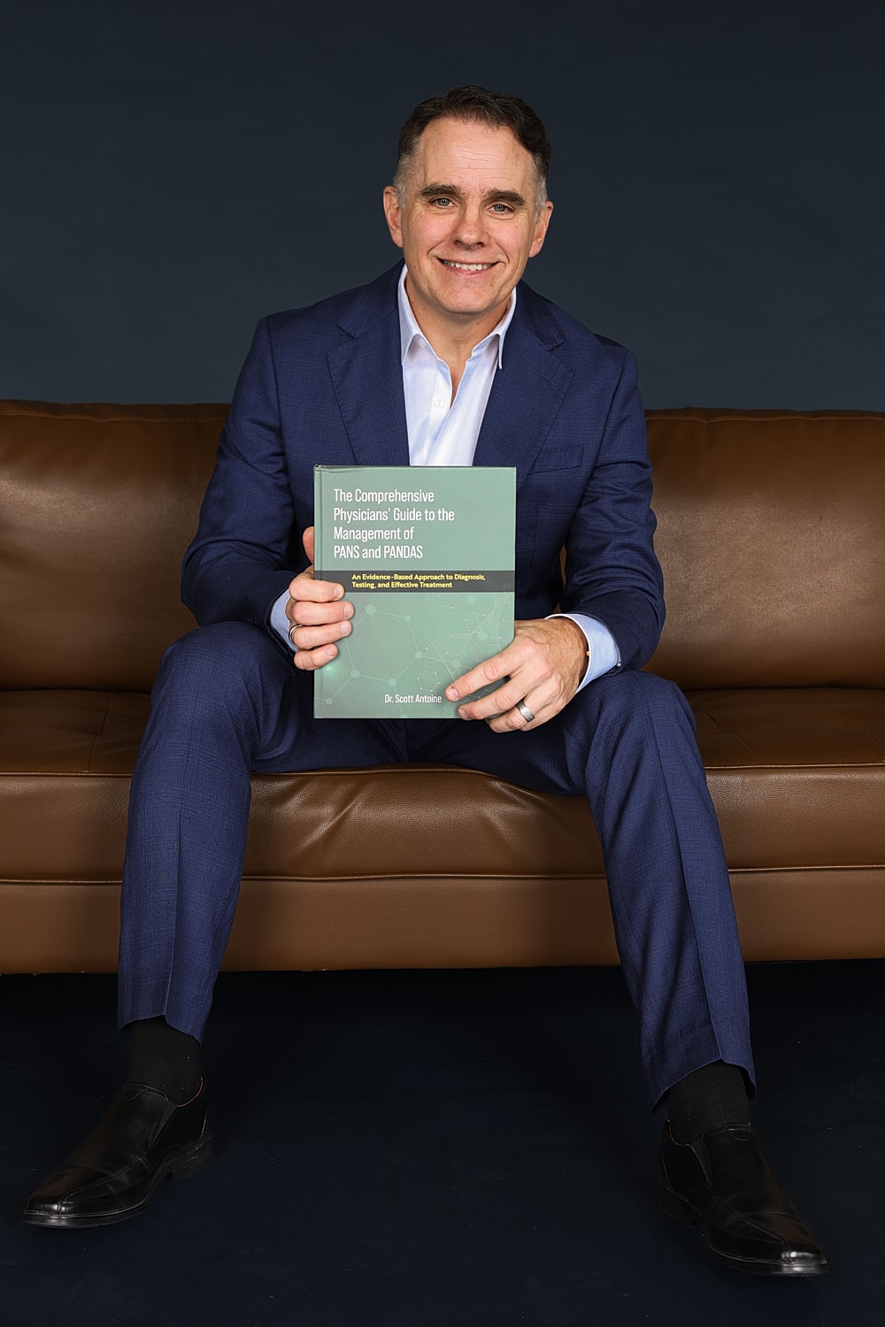 Man in suit holding medical book on couch.