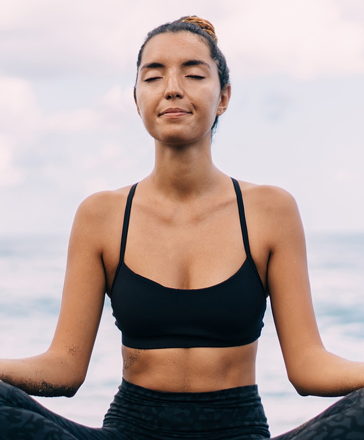 Woman meditating by the ocean, peaceful expression.