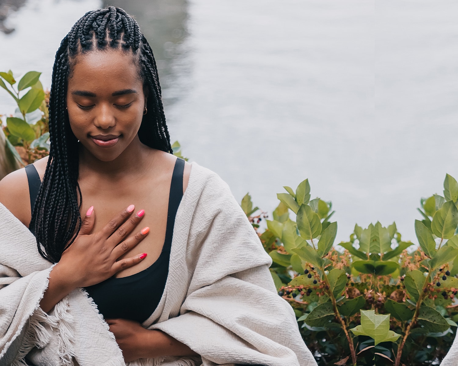 Woman meditating by water, surrounded by greenery.