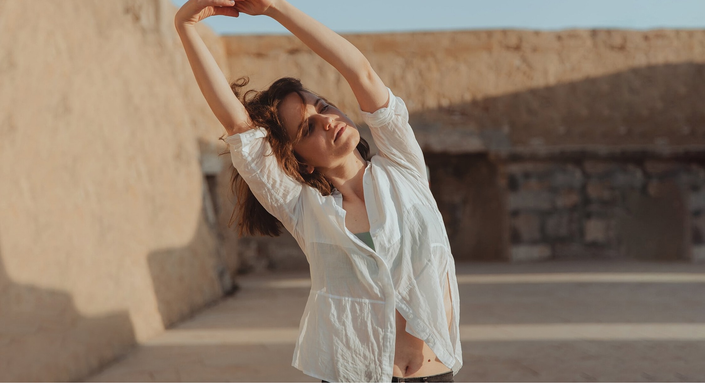 Woman stretching in a sunlit outdoor setting.