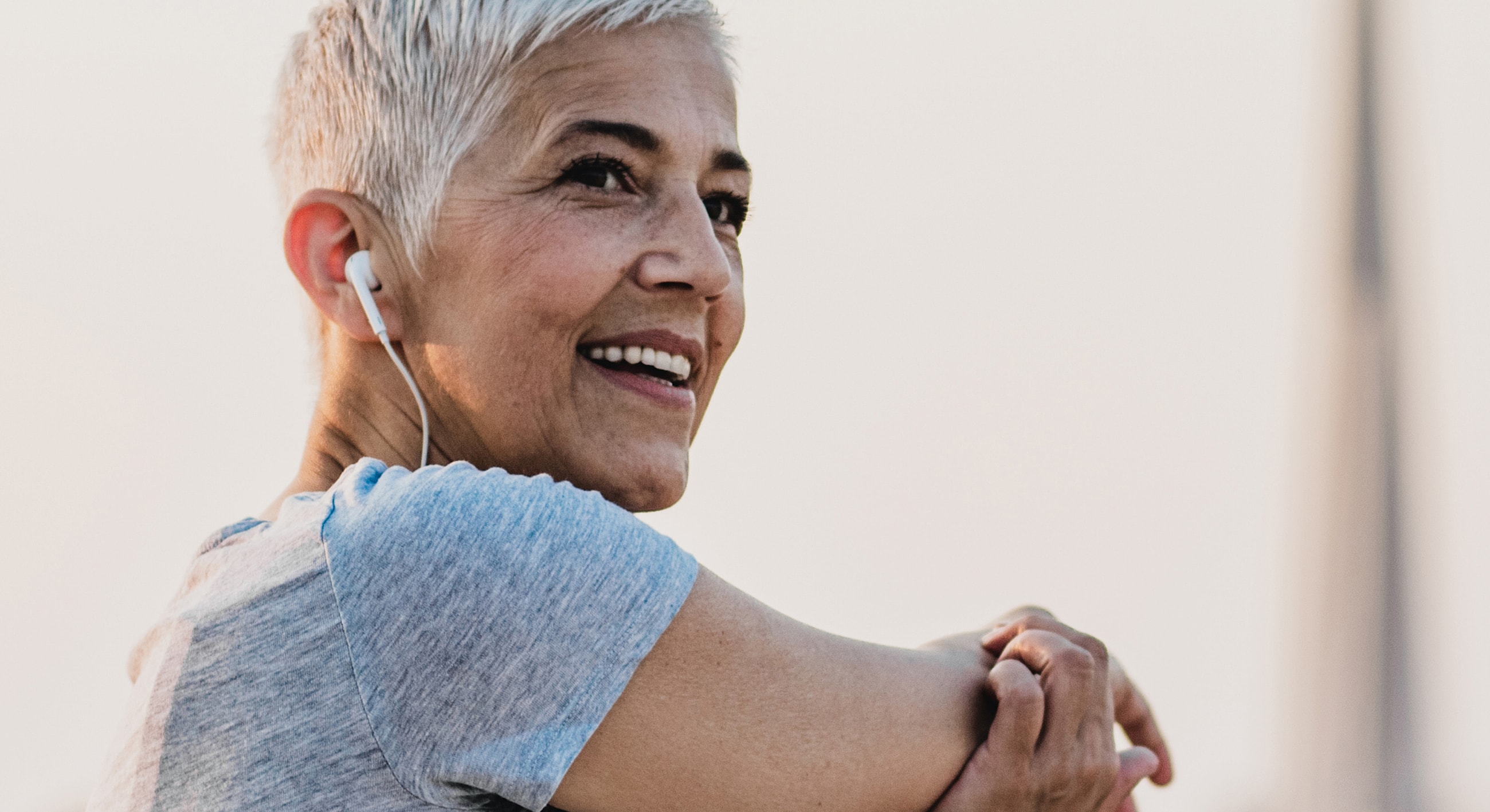 Smiling woman stretching with earbuds outdoors.