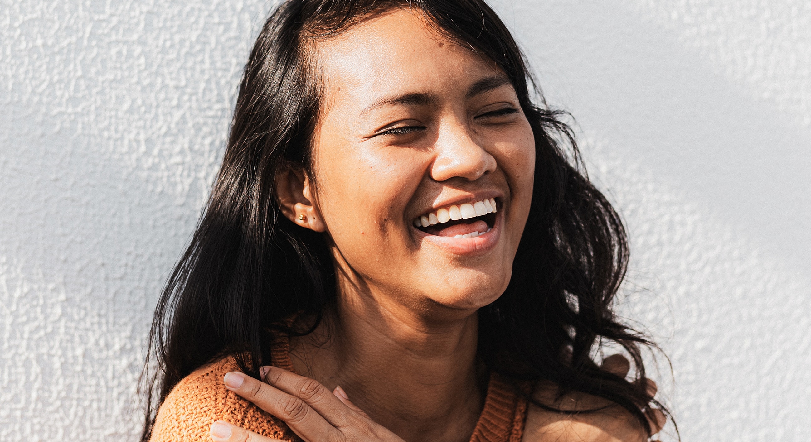 Woman laughing against a textured white background.